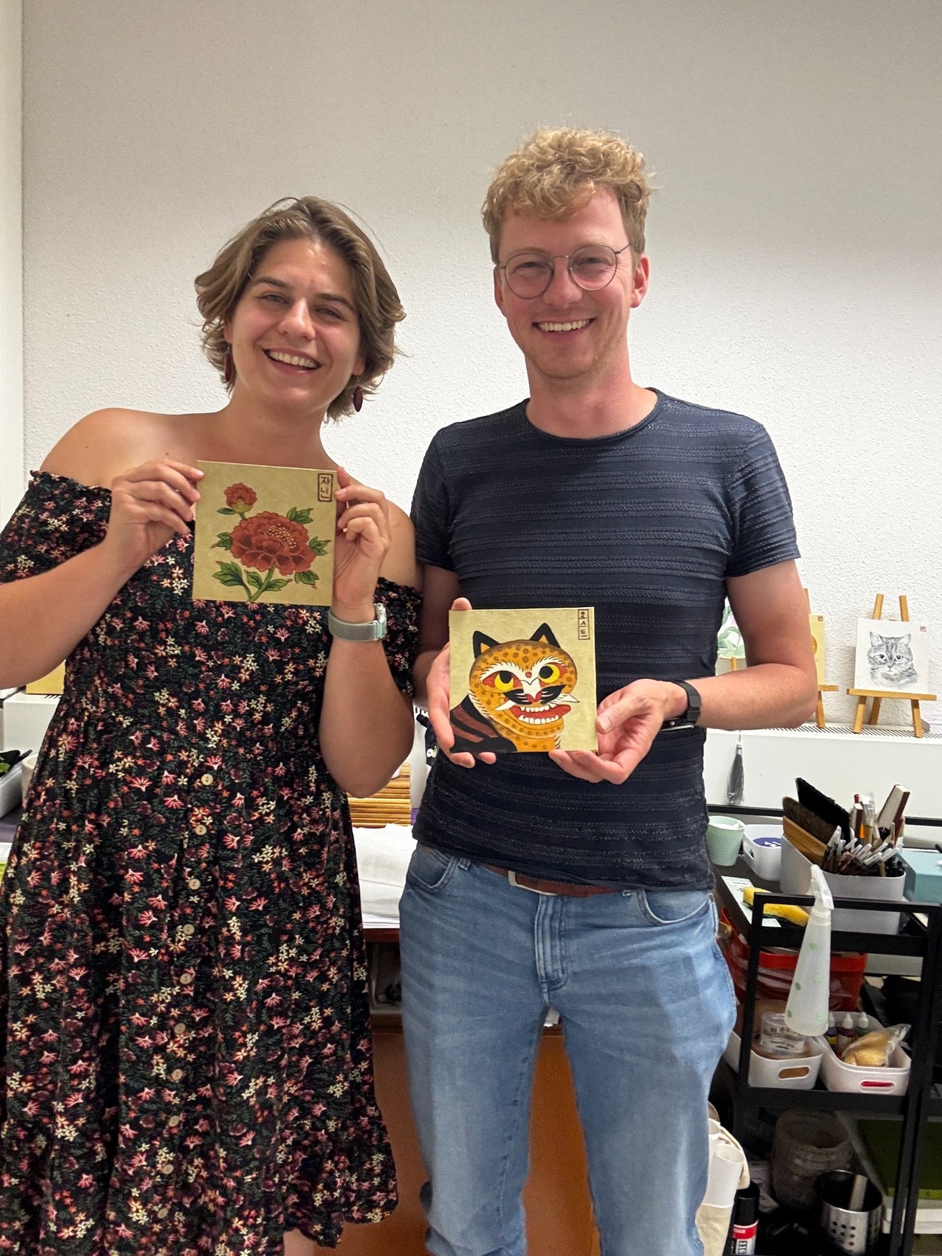 Two students smiling and holding finished Minhwa paintings